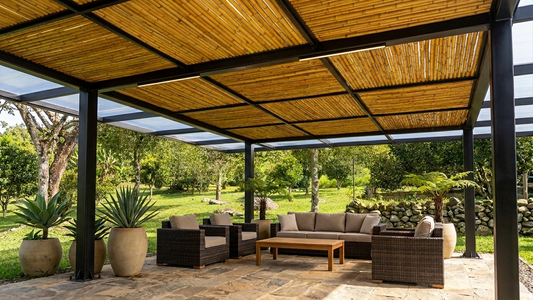Pérgola moderna con estructura metálica negra y techo de cañas de guadua natural en una terraza con sala exterior.